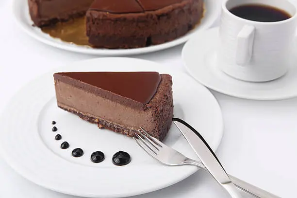Foto de uma fatia de cheesecake de chocolate em um prato branco ao lado de uma xícara de café