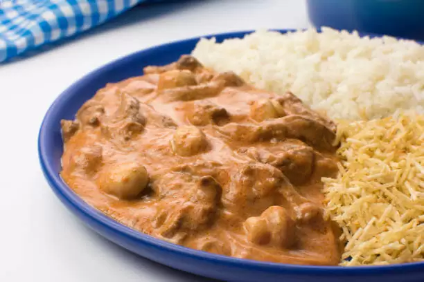 Estrogonofe de carne em um prato azul acompanhado de arroz e batata palha